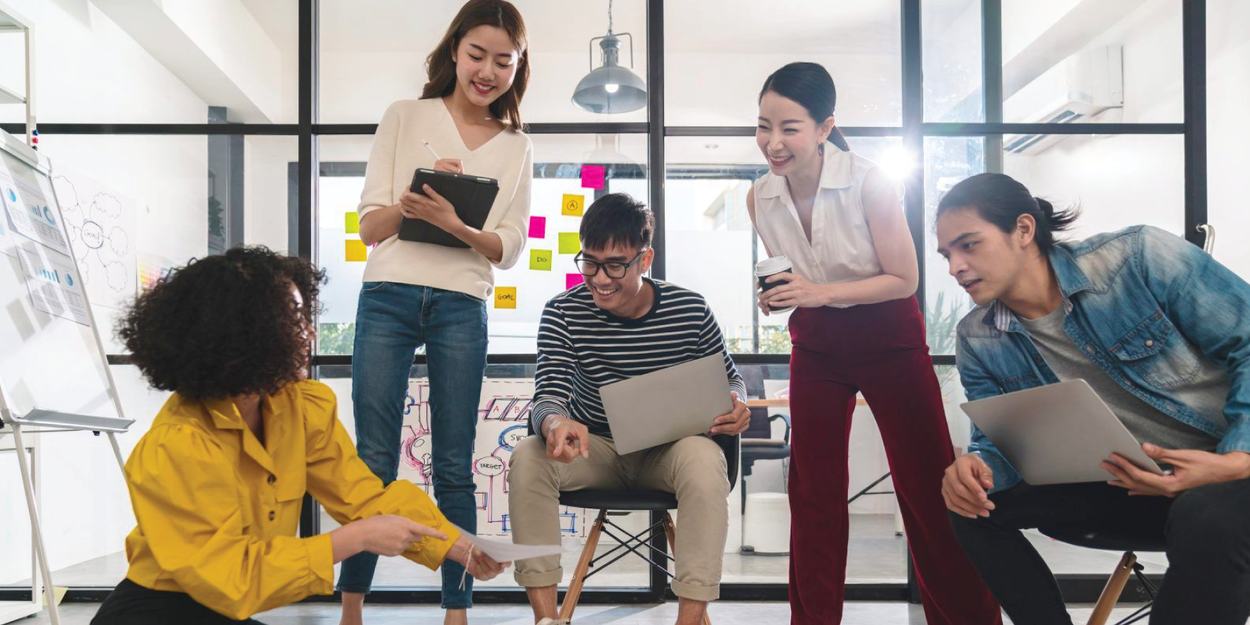 Young creative asian group meeting and looking at project plan lay out on floor discuss or brainstorm business strategy with post note workshop for startup team in small office happy workplace