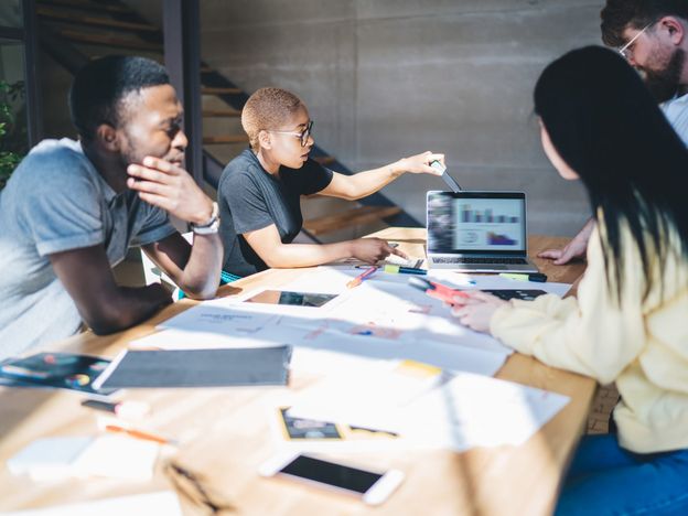 Black woman presenting charts on laptop during meeting with colleagues