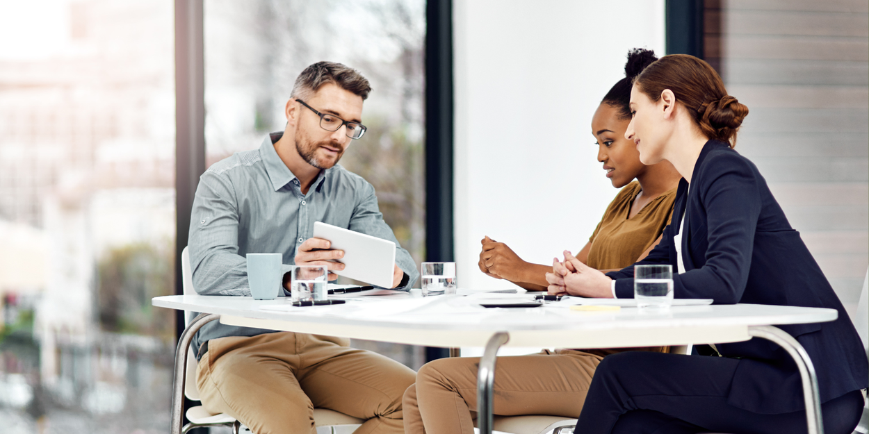 Three employees sitting around a desk talking