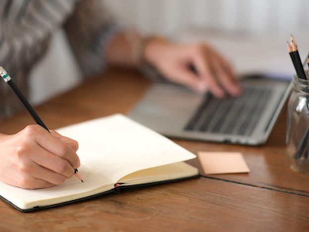Businesswoman writing note while using laptop at table in office