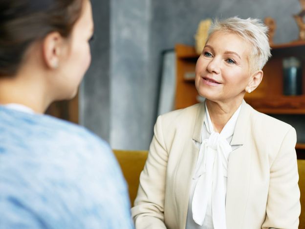 Psychology consulting and coaching concept stylish middle aged female psychologist having conversation with brunette woman client discussing problems and progress sitting in her cozy office