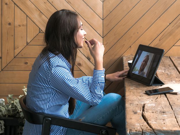 Beautiful cute caucasian young female with long black hair in rustic cafe having a video call with a friend