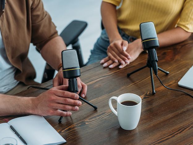 Cropped view of two radio hosts sitting at workplace near microphones