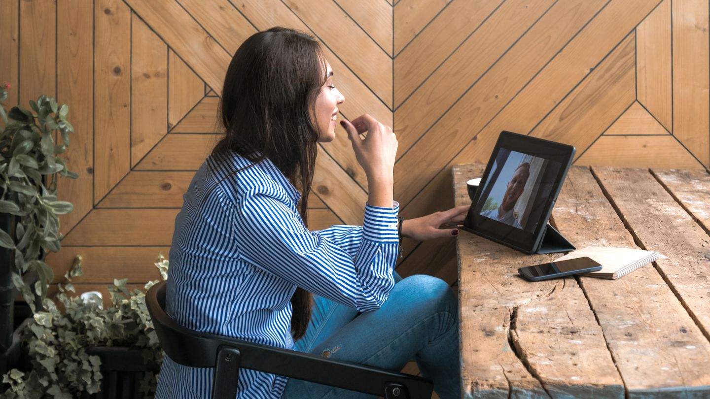 Beautiful cute caucasian young female with long black hair in rustic cafe having a video call with a friend