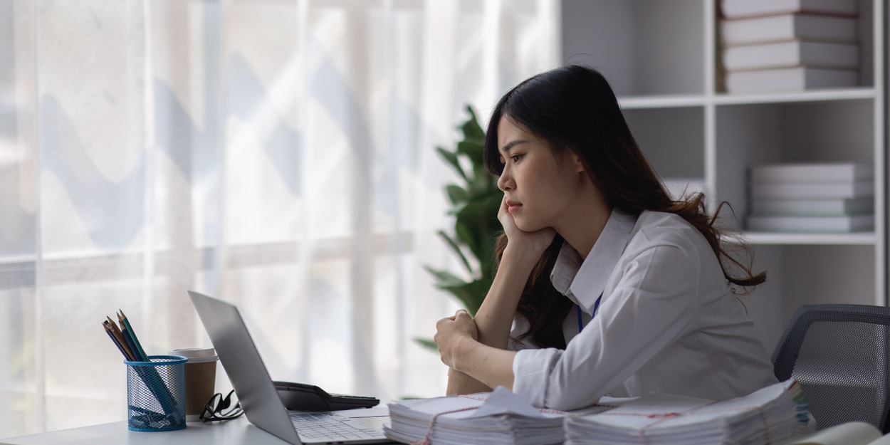 Stressed employee with a stack of work next to her