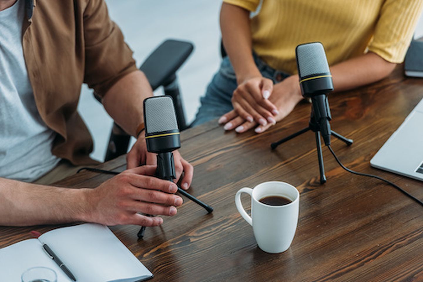 Cropped view of two radio hosts sitting at workplace near microphones