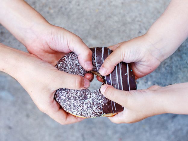 Childrens hands holding a chocolate donut two kids pull to themselves donut closeup the concept of sharing food