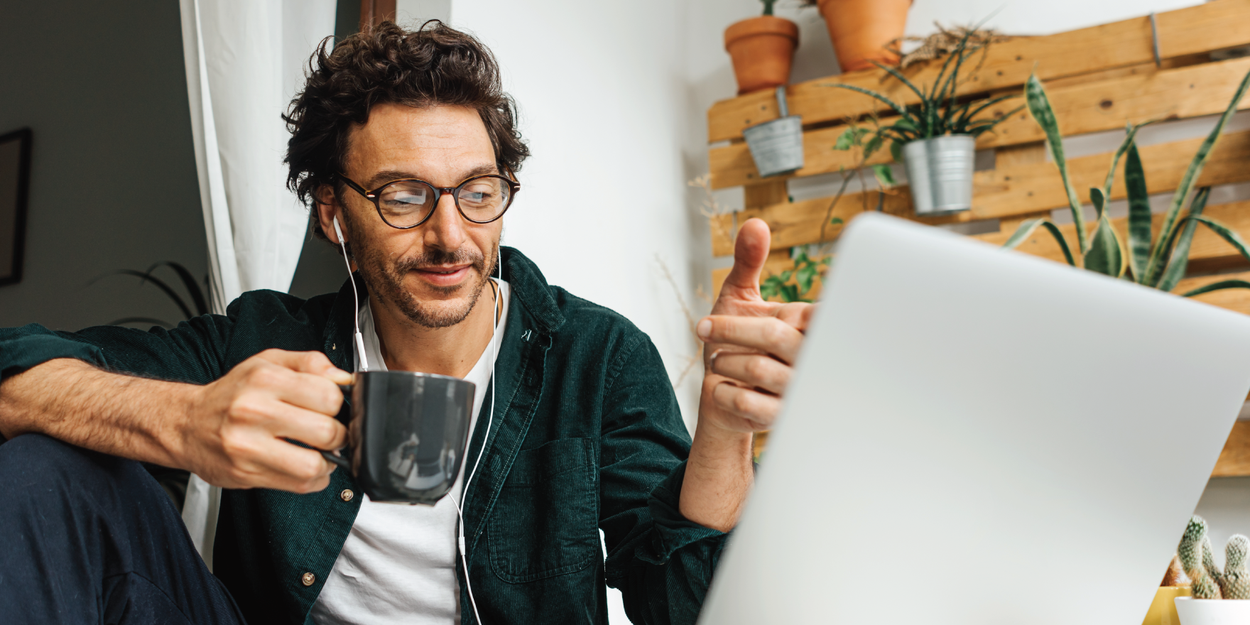 Man using laptop with headphones holding a mug