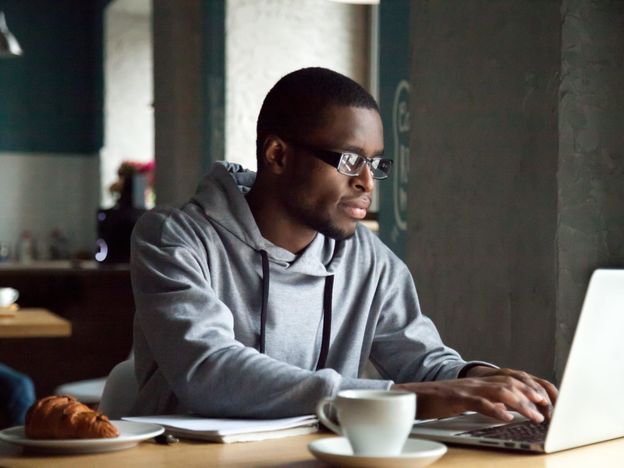 Serious millennial african american man using laptop sitting at
