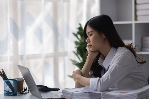 Stressed employee with a stack of work next to her